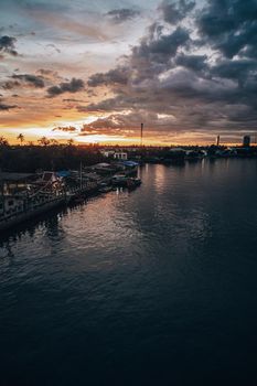 Panorama Cityscape at sunset with large river at foreground and strom clouds at background in Thailand.