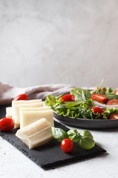 A piece of fresh sliced halloumi on a slate board with cherry tomatoes and spinach leaves. Preparing to cook cheese on the grill. Copy space.