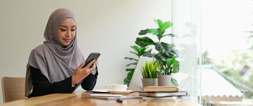 Happy asian muslim woman holding mobile phone cellular at her office