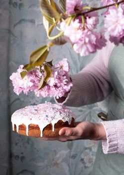 a woman decorates a homemade Easter cake with pink sakura flowers, spring blossom, a bouquet of pink sakura flowers on a table in a decorated spring room, a beautiful still life. High quality photo