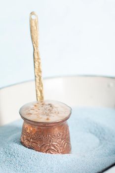 copper coffee pot with hot coffee on blue sand and blue background, beautiful blue color, coffee break, turkish coffee. High quality photo