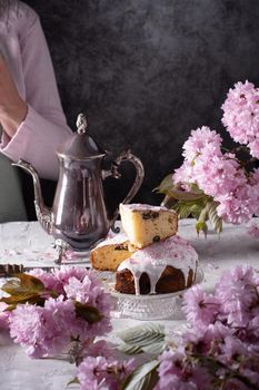 a woman decorates a homemade Easter cake with pink sakura flowers, spring blossom, a bouquet of pink sakura flowers on a table in a decorated spring room, a beautiful still life. High quality photo