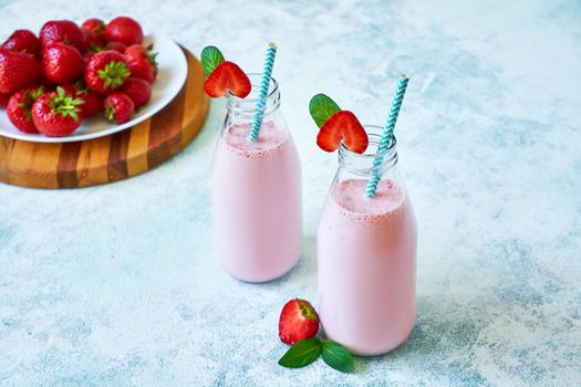 Strawberry smoothie or milkshake in glass jar with berries on blue concrete background. Healthy summer drink.