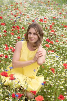 a beautiful young blonde woman in a yellow dress stands among a flowering field of poppies, daisies, cornflowers and laughs. High quality photo