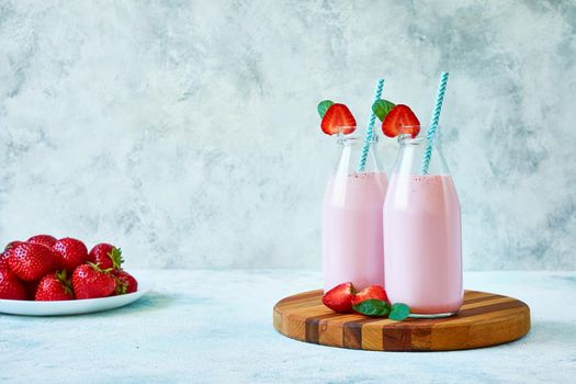 Refreshing healthy summer drink. Strawberry smoothie or milkshake in glass jar with berries on blue concrete background.