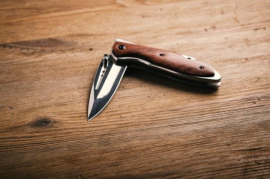 stainless steel folding knife isolated over wood background