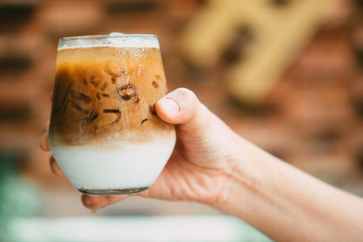 Hand hold iced latte coffee in a glass with cream on bottom . cold summer drink background