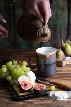 cheese plate with goat cheese, grapes and figs, copper teapot, angle view, healthy food, high-calorie breakfast. High quality photo