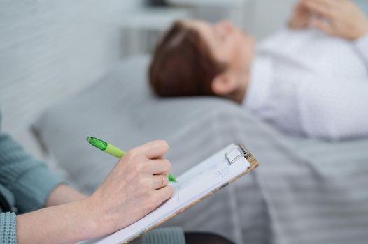 A caucasian woman lies on a couch and expresses her feelings, while a psychologist makes notes on a tablet