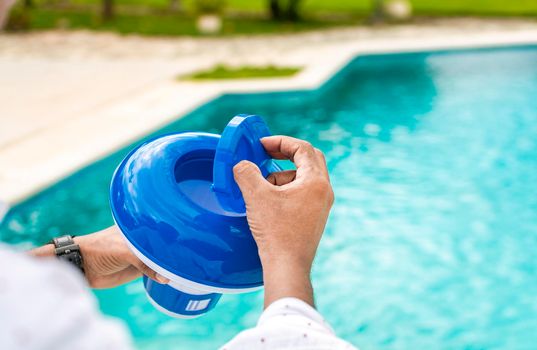 Hands of a worker installing a pool chlorine float, a person holding a pool chlorine dispenser. Hands holding a pool chlorine dispenser. Hand of a pool disinfection worker holding a chlorine dispenser.