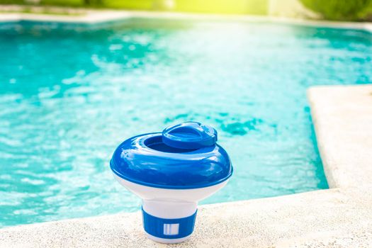 A chlorine dispenser for swimming pools with blue water in the background. Dosing float for swimming pool chlorination, A chlorine float on the edge of a swimming pool. 