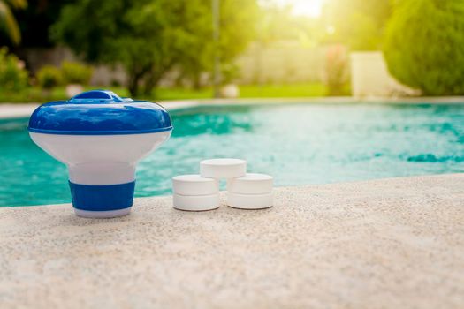 Tablets with chlorine dispenser for swimming pools. Chlorine tablets with dosing float, Pool float and chlorine tablets, A pool float and chlorine tablets on the edge of a swimming pool.