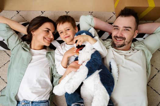 Happy family lying on the floor in new home with cordboard boxes around, close up