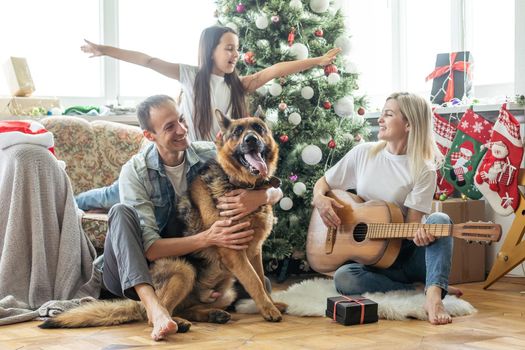 smiling family and daughter with dog sitting near christmas tree with gifts.