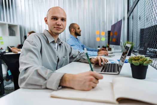 Young bald business man sitting at desk in office, working on computer, close up