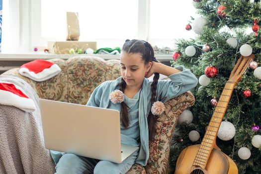 Christmas distance learning online education. Schoolgirl studying at home with laptop notebook and doing school homework.