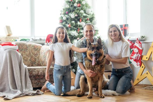 Friendly family is playing with dog near Christmas tree. They are sitting and laughing.