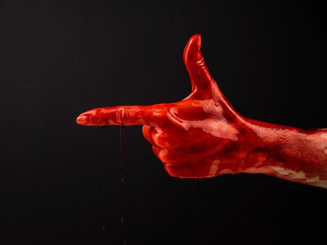 Woman's hand in blood shows a gesture of a gun on a black background