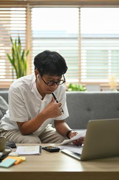 Focused young man calculating expenses and managing household family budget in living room.