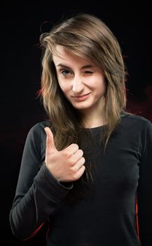 Teenage girl squinting with one eye and shows the symbol OK. Fashion, portrait and people concept. Portrait of a young emotional woman on a dark background