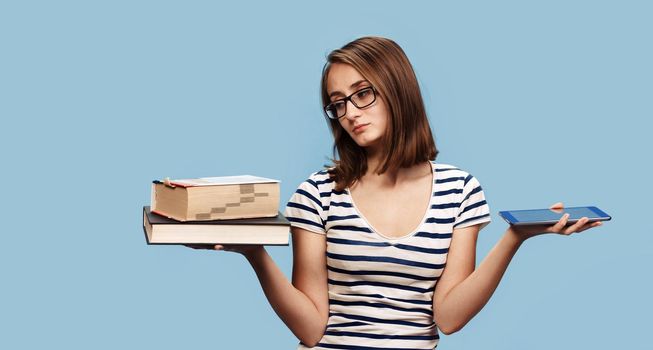 Contemporary education concept. Book vs e-book. Girl student holding traditional textbook and ebook reader on background with copy space. The choice between paper books and electronic gadgets. 