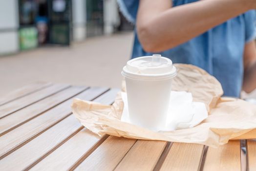 Summer vacation, street food eating. closeup of woman eating fast food in street cafe, mockup white coffee cup, focus on foreground