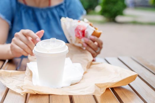 Summer vacation, street food eating. closeup of woman eating fast food in street cafe, mockup white coffee cup, focus on foreground