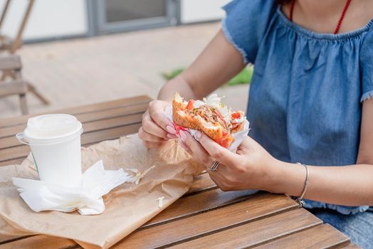 Summer vacation, street food eating. closeup of woman hands holding hamburger, woman eating fast food at street cafe