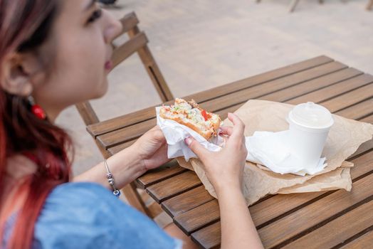 Summer vacation, street food eating. closeup of woman hands holding hamburger, woman eating fast food at street cafe, view from behind