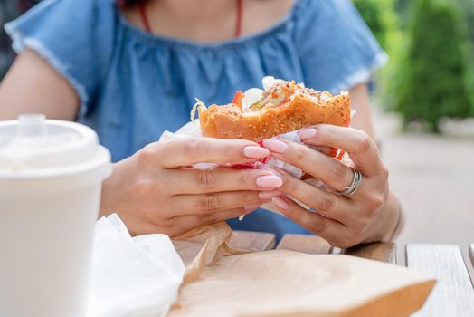 Summer vacation, street food eating. closeup of woman hands holding hamburger, woman eating fast food at street cafe