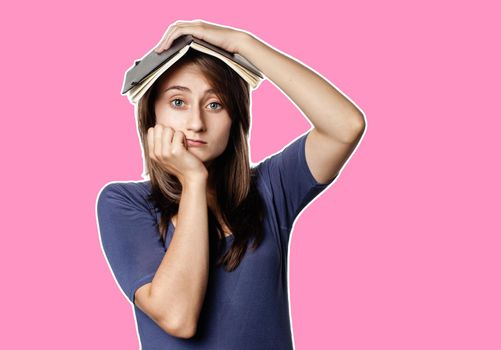 Education and lifestyle concept. Tired girl holds a notebook on her head on a white background. Magazine style collage with copy space and pink background