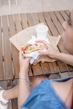 Summer vacation, street food eating. closeup of woman hands holding hamburger, woman eating fast food at street cafe, view from behind