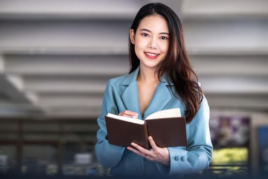 Asia woman entrepreneur or businesswoman showing a smiling face while reading a book developing financial and investing strategies