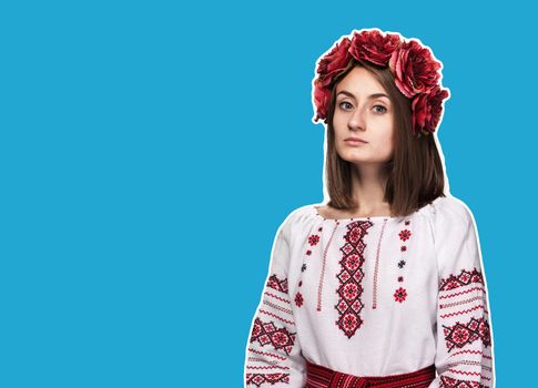 Beautiful sad girl in the Ukrainian national suit. Magazine style collage on blue background with copy space