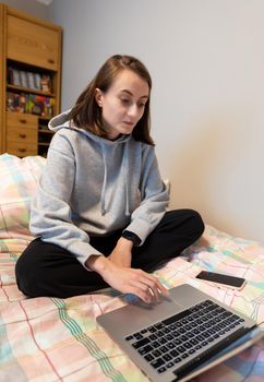 Home office and remote work concept. A young woman works on a computer remotely at home while sitting on a couch during the coronavirus pandemic.