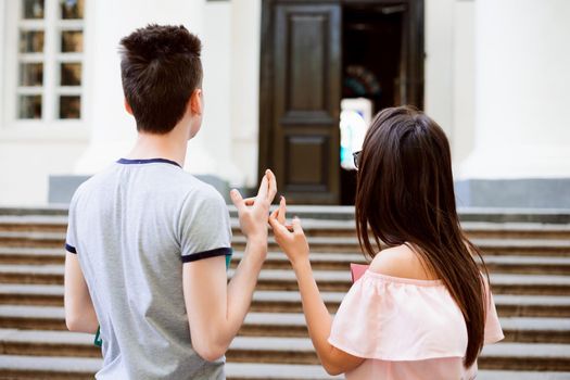 Students crossing fingers before taking entrance examination to the university standing in front of their dreamed institution and looking at entrance door