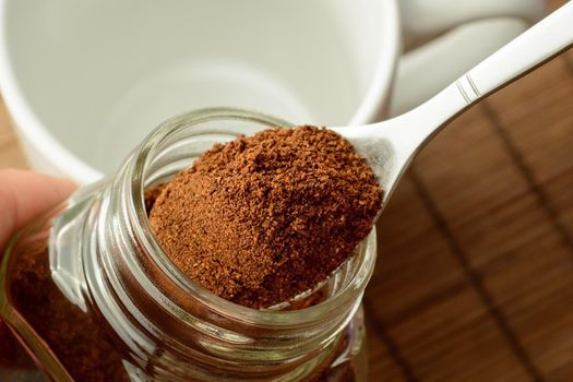 Man`s hand taking some ground coffee from coffee jar