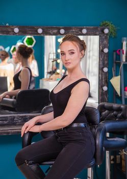 A girl on a chair with a new make-up and hairstyle looks at the camera. A new look for a young woman. Business concept - beauty salon, facial skin and hair care.