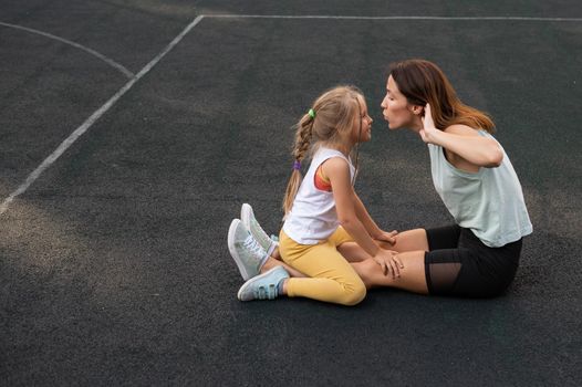 Mother and daughter go in for sports outdoors. Caucasian woman and little girl are engaged in fitness at the stadium