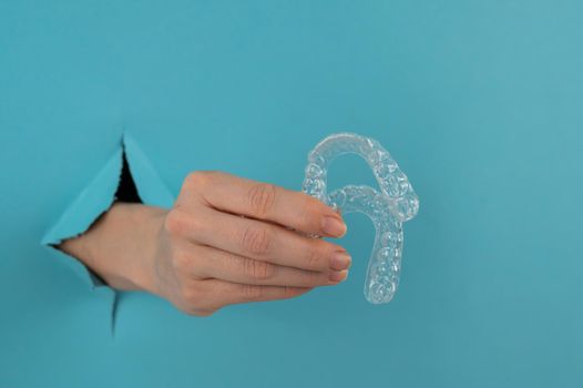 A female hand sticking out of a hole from a blue background holds removable night retainers