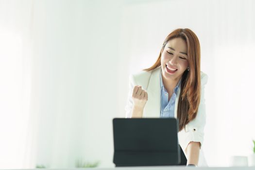 Portrait of a successful Asian businesswoman or business owner expressing excitement and joy using a tablet computer in the office.