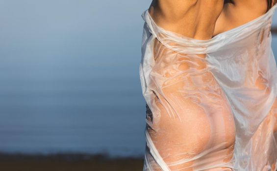 Beautiful naked girl outdoors enjoying nature. Two young nude women wrapped in white shawl posing on sea background. Sexy naked brunettes enjoying summer time outdoors. View from the back