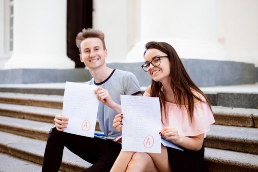 Portrait of college students sitting on stairs and showing perfect test results