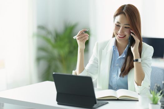 Portrait of an Asian businesswoman or business owner smiling and talking on a mobile phone in the office.