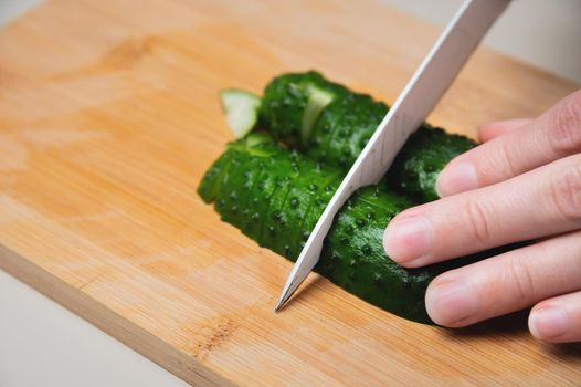 Close-up of female hands cutting fresh cucumber on cutting board at home kitchen.