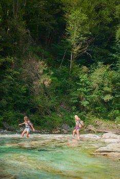 Two young friends crossing a river on a travel adventure exploring nature together. Carefree women walking across rocks in a lake, having fun on a summer vacation.
