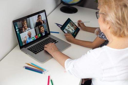 Happy mature grandmother with adorable little granddaughter using tablet at home together, excited middle aged woman and cute kid looking at device screen.