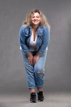 Beautiful plump woman in a denim suit on a gray background.