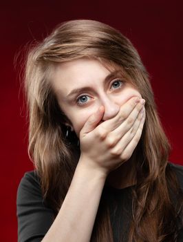 Teenage girl covers her mouth with a hand. Fashion, portrait and people concept. Portrait of a young emotional woman on a dark background