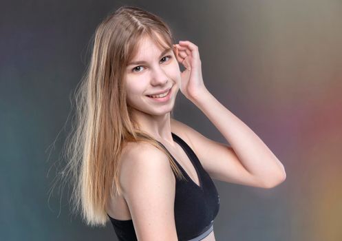 A beautiful teenage girl in a sports undershirt on a gray background looks at the camera and smiles.